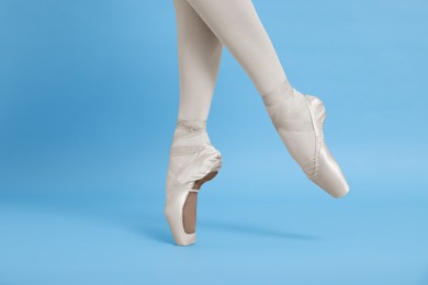 Photo of Young ballerina in pointe shoes practicing dance moves on light blue background, closeup