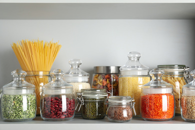 Photo of Glass jars with different types of groats and pasta on white shelf