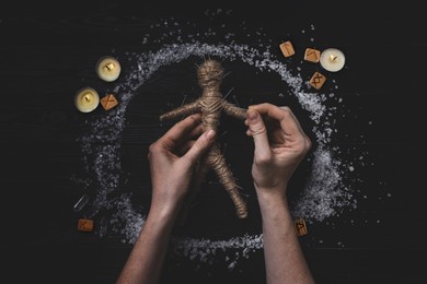 Image of Woman stabbing voodoo doll with pins at wooden table, top view