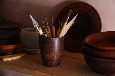 Set of different crafting tools and clay dishes on wooden table in workshop