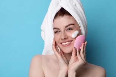 Young woman washing face with brush and cleansing foam on light blue background