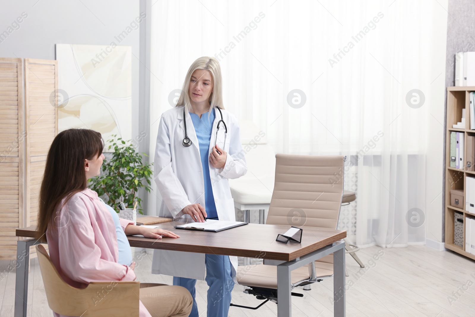 Photo of Doctor consulting pregnant patient at table in clinic