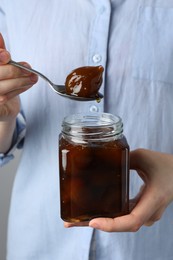 Photo of Woman holding jar of tasty sweet fig jam, closeup