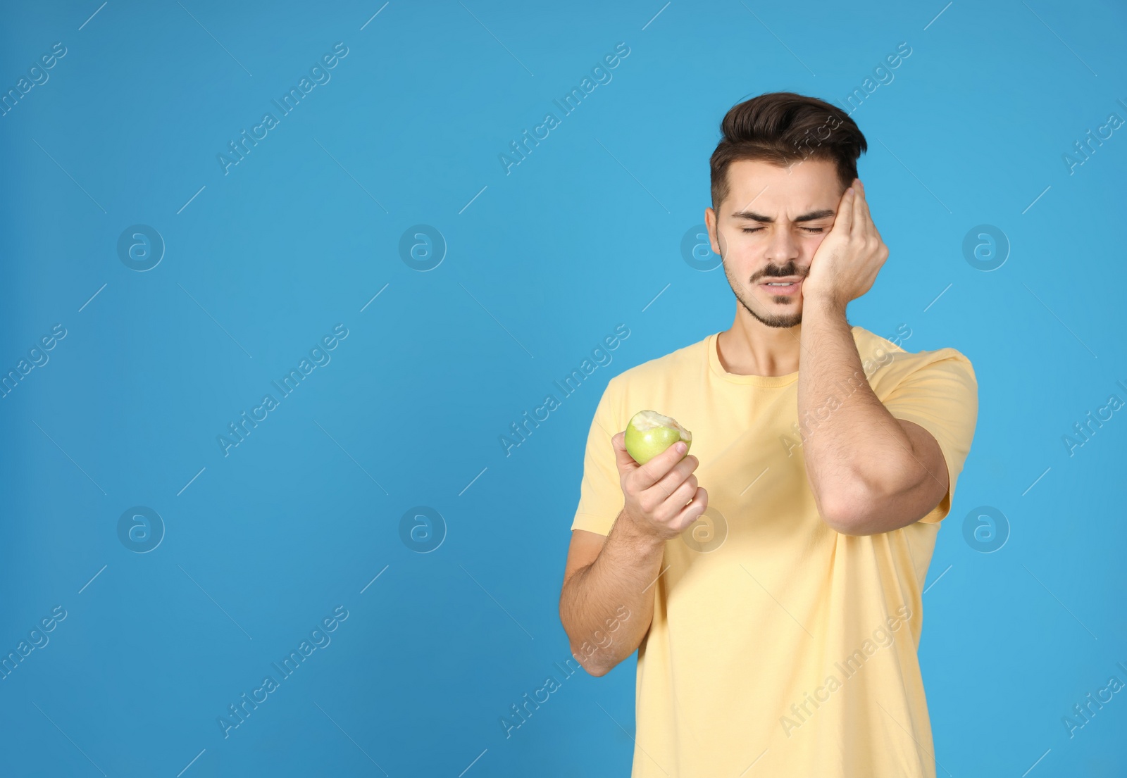 Photo of Emotional young man with sensitive teeth and apple on color background. Space for text