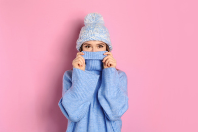 Young woman wearing warm sweater and hat on pink background. Winter season