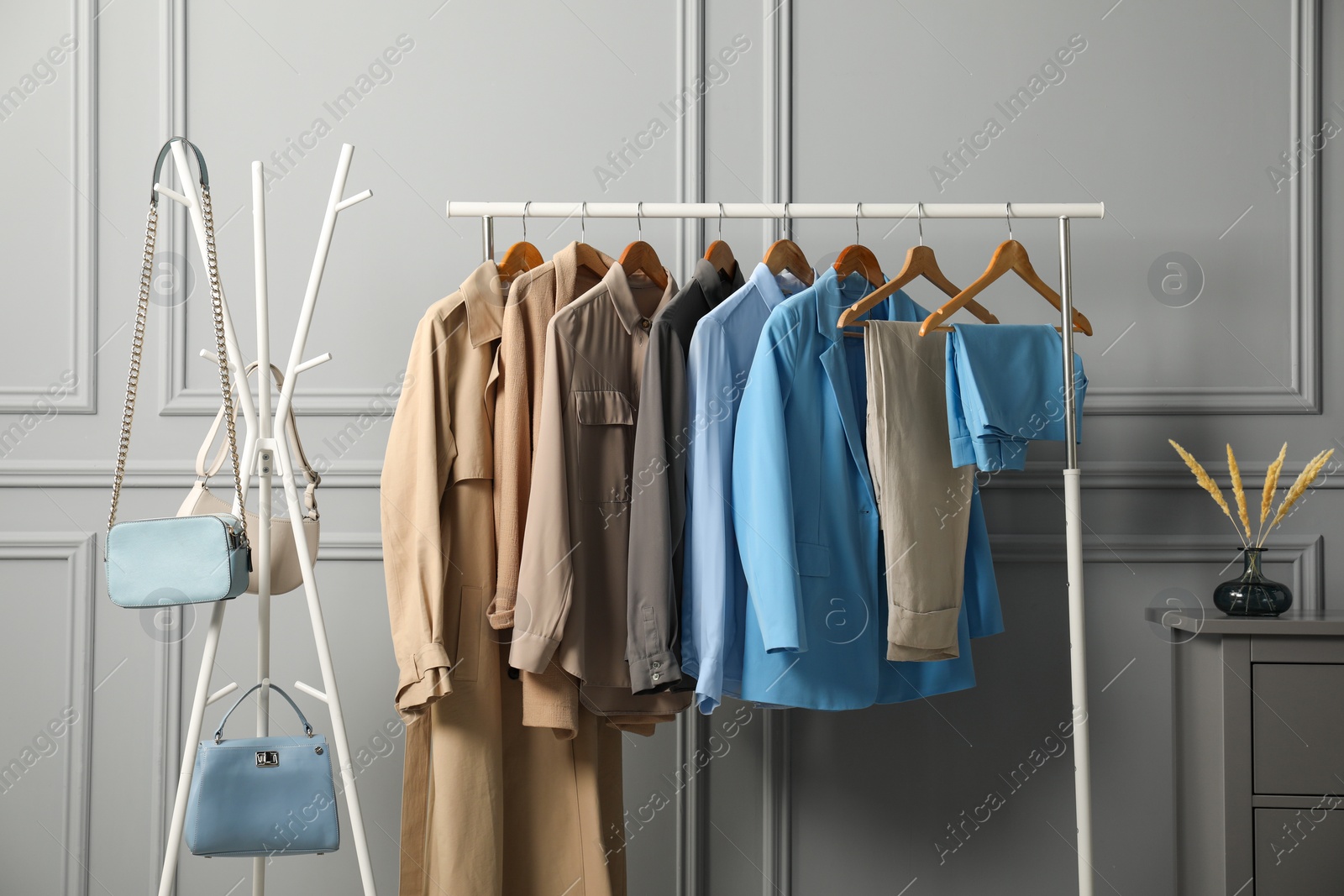 Photo of Rack with different stylish women`s clothes and bags near grey wall