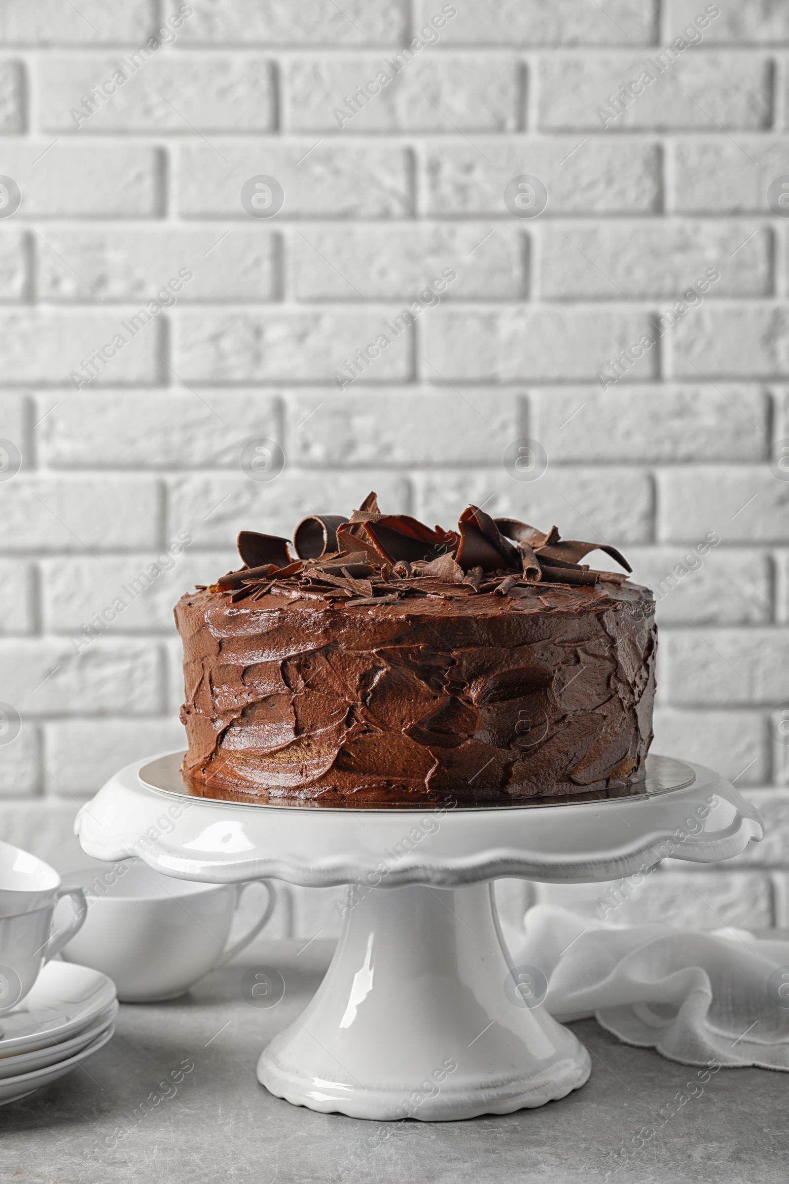 Photo of Stand with tasty homemade chocolate cake on table near white brick wall. Space for text