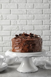 Stand with tasty homemade chocolate cake on table near white brick wall. Space for text