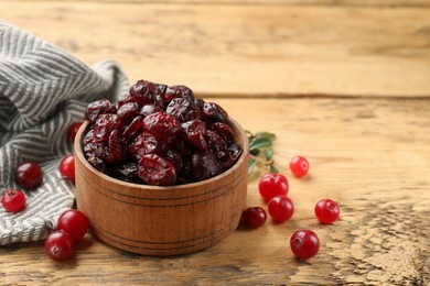 Photo of Tasty dried cranberries in bowl and fresh ones on wooden table, closeup. Space for text