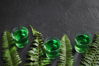 Photo of Absinthe in shot glasses and green leaves on black table, space for text. Alcoholic drink