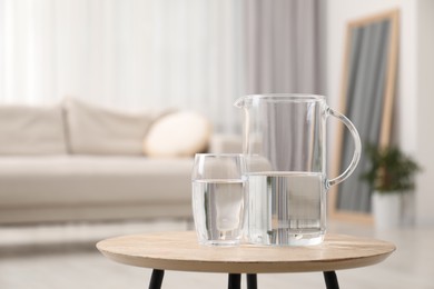 Photo of Jug and glass with clear water on wooden table indoors. Space for text