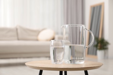 Jug and glass with clear water on wooden table indoors. Space for text