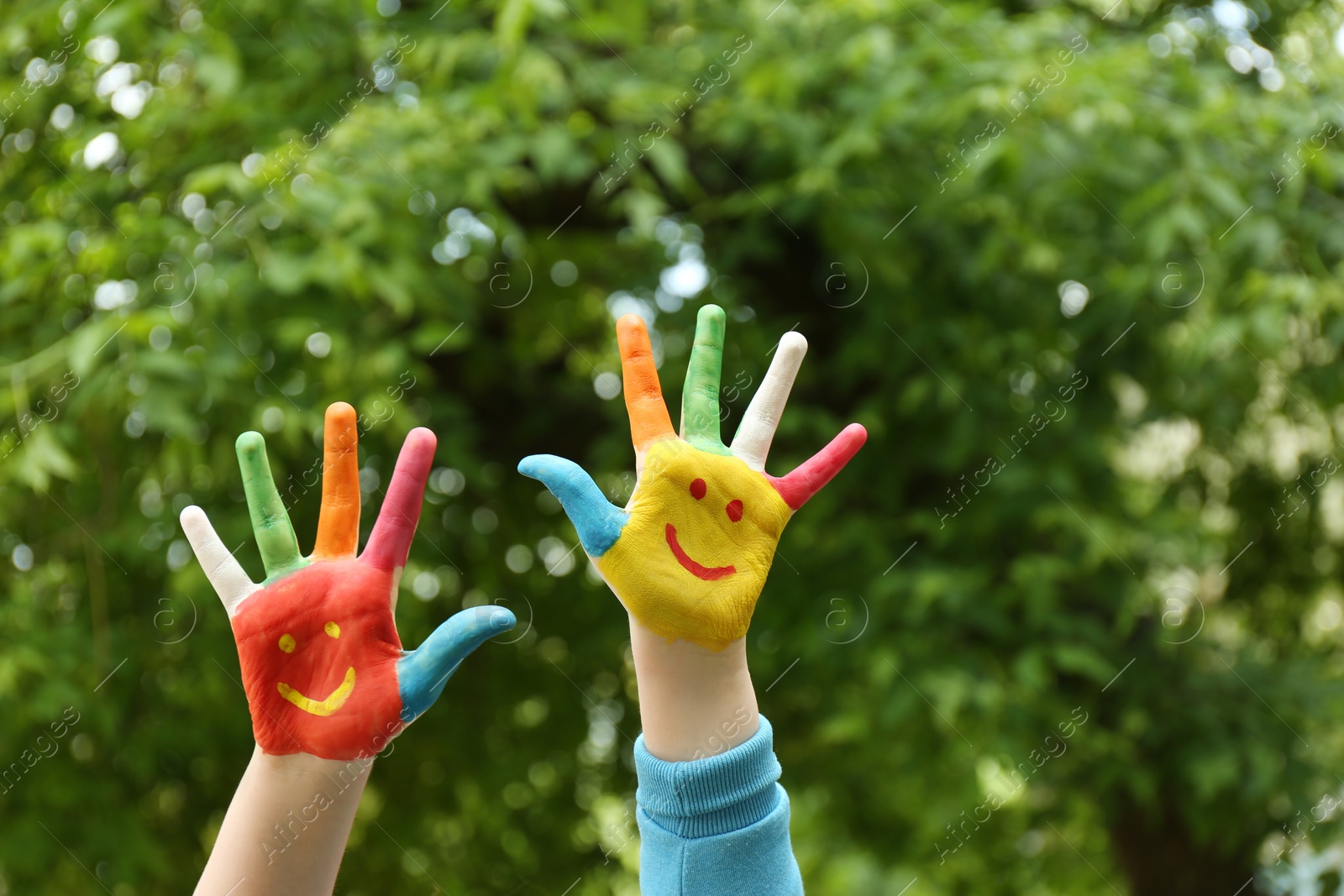 Photo of Kid with smiling faces drawn on palms in green park, closeup