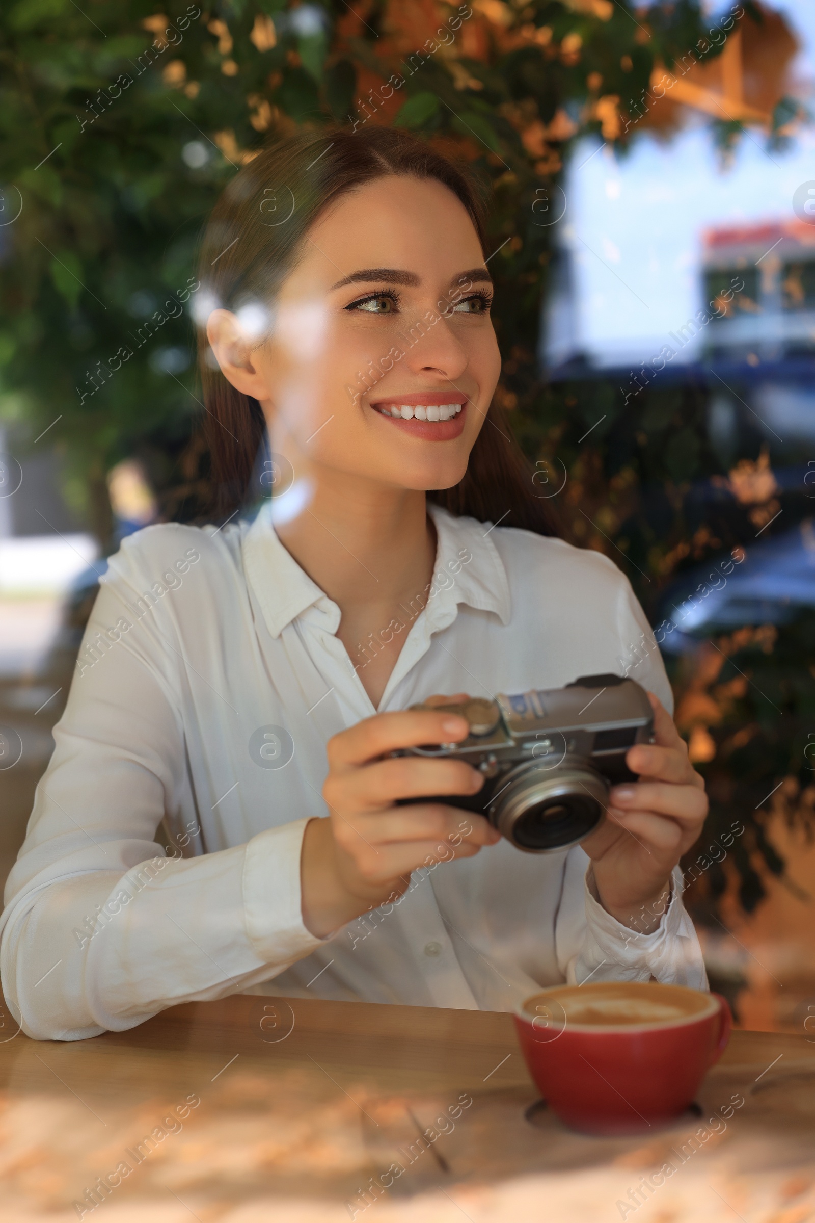 Photo of Young woman taking photo of cup with coffee at cafe, view through window. Creative hobby