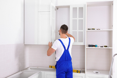 Photo of Worker installing door of cabinet with screwdriver in kitchen