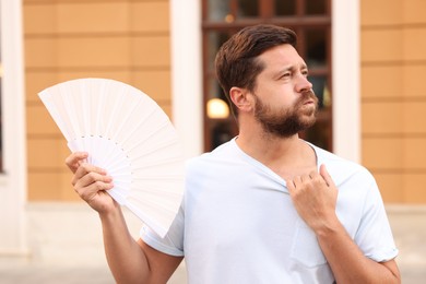 Photo of Man with hand fan suffering from heat outdoors