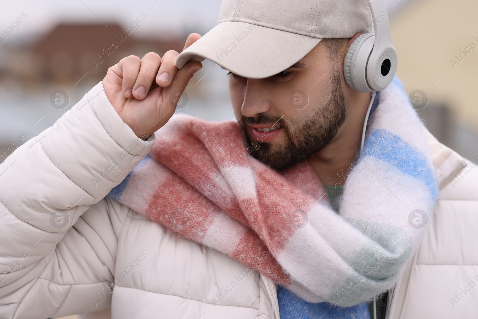 Photo of Handsome man in warm scarf and headphones on blurred background