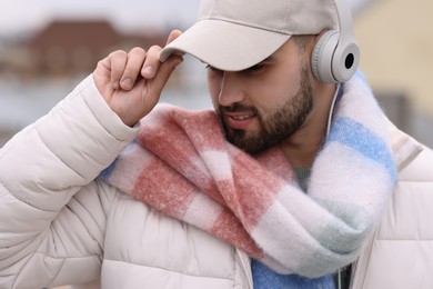 Photo of Handsome man in warm scarf and headphones on blurred background