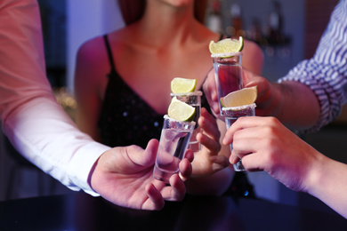 Photo of Young people toasting with Mexican Tequila shots at bar, closeup