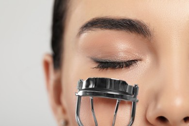 Photo of Young woman using eyelash curler on light grey background, closeup