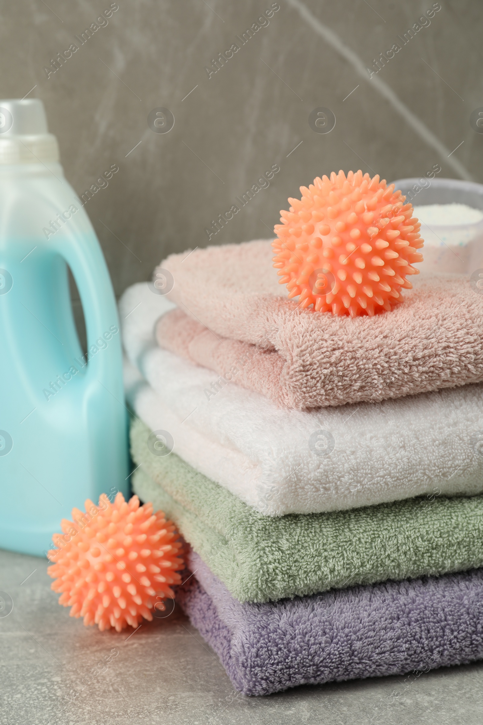 Photo of Dryer balls, detergents and stacked clean towels on grey marble table