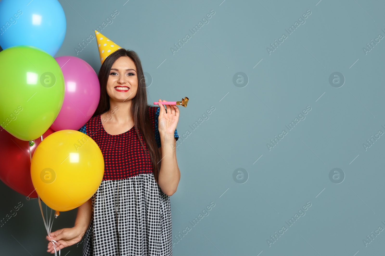 Photo of Young woman with bright balloons and party blower on color background. Birthday celebration