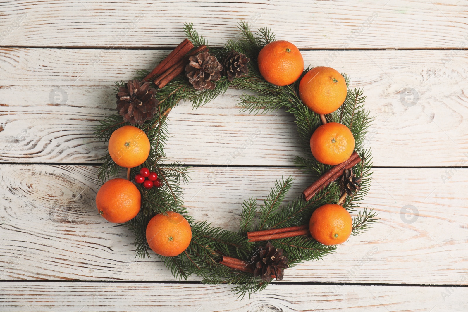 Photo of Decorative wreath with tangerines, fir tree branches and spices on wooden background, top view