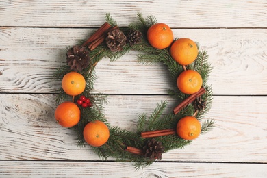 Decorative wreath with tangerines, fir tree branches and spices on wooden background, top view