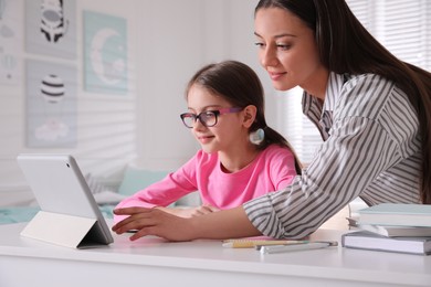 Mother helping her daughter doing homework with tablet at home