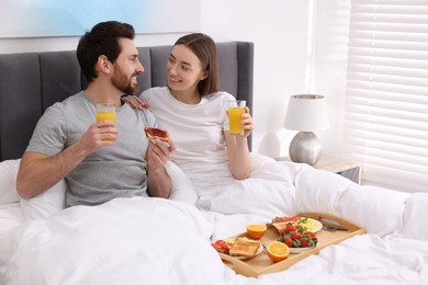 Happy couple eating tasty breakfast in bed at home