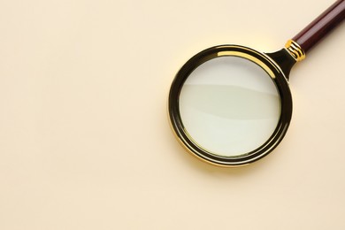 Magnifying glass on beige background, top view. Space for text