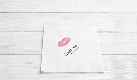 Paper napkin with lipstick mark and words CALL ME on wooden background. Space for text