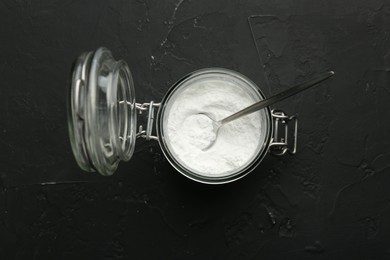 Baking powder in jar and spoon on black textured table, top view