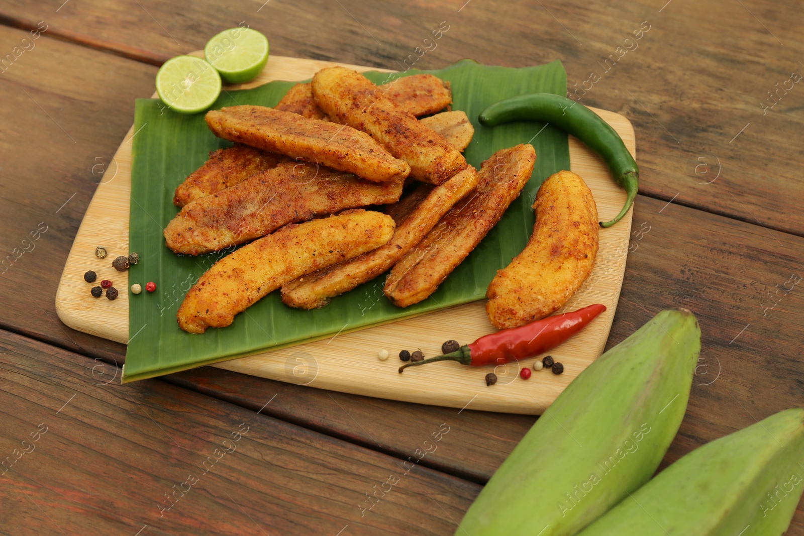 Photo of Delicious fried bananas, fresh fruits and different peppers on wooden table