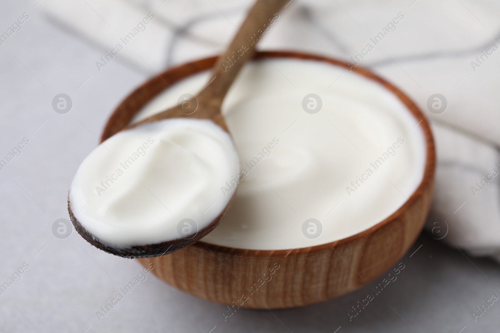 Photo of Delicious natural yogurt in bowl and spoon on light grey table, closeup