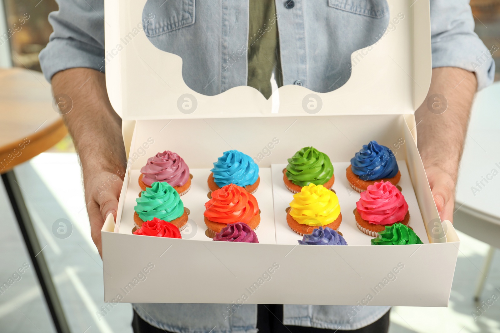 Photo of Man holding box with delicious colorful cupcakes indoors, closeup