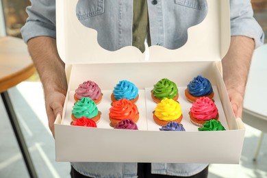Man holding box with delicious colorful cupcakes indoors, closeup