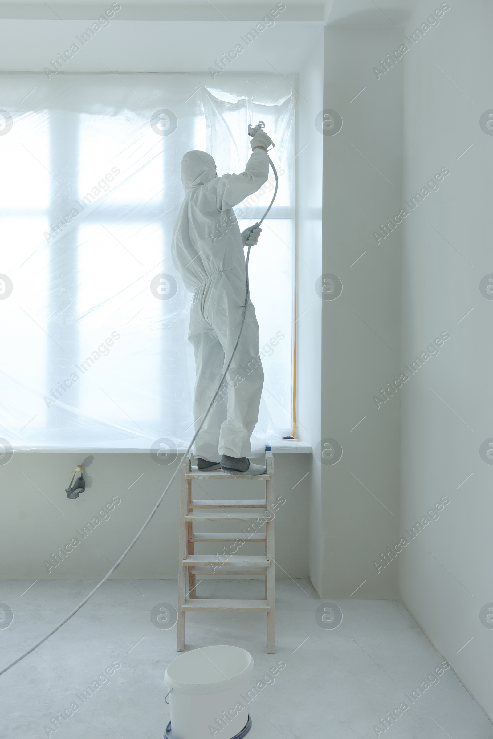 Photo of Decorator painting window slope on ladder indoors, back view