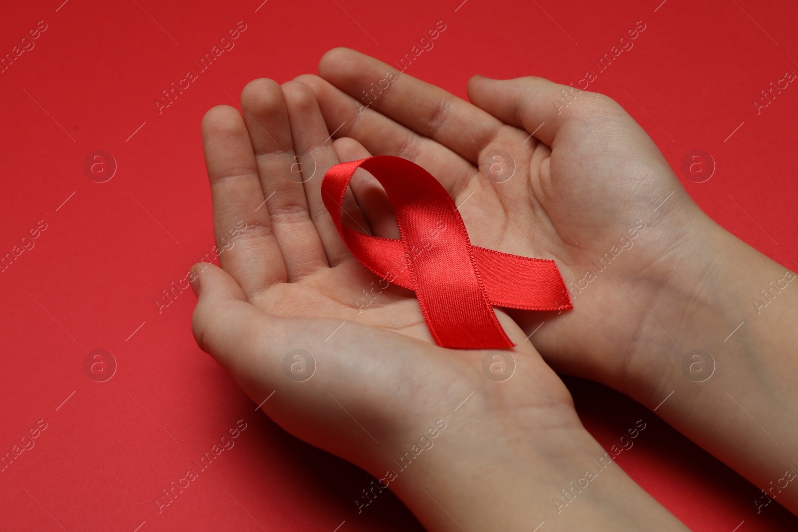 Photo of Little girl holding red ribbon on bright background, closeup. AIDS disease awareness