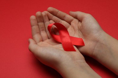 Little girl holding red ribbon on bright background, closeup. AIDS disease awareness