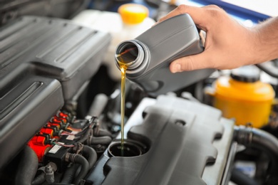 Photo of Mechanic pouring oil into car engine, closeup