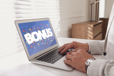 Image of Bonus gaining. Man using laptop at white table indoors, closeup. Illustration of falling confetti and word on device screen