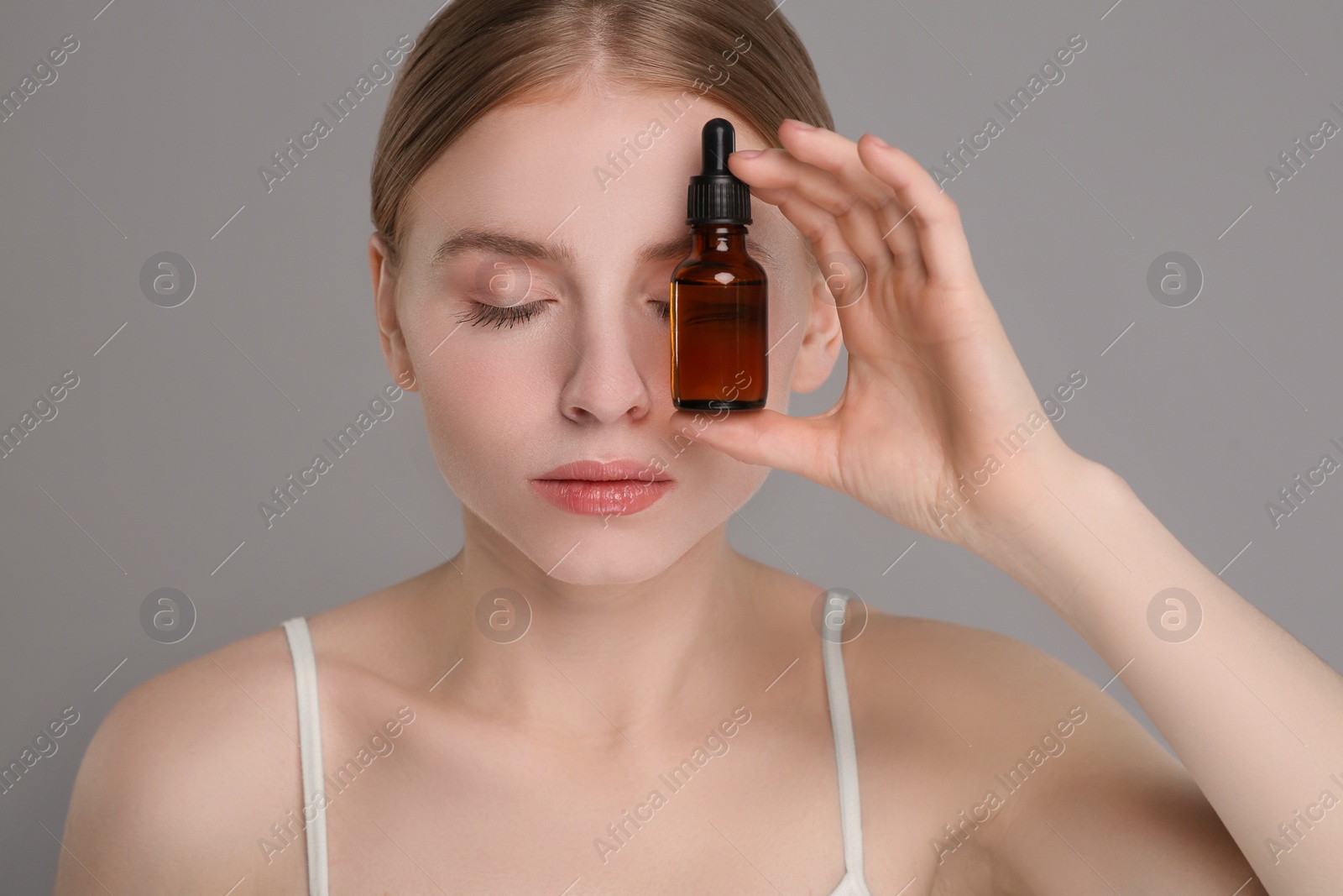 Photo of Beautiful young woman with bottle of essential oil on light grey background