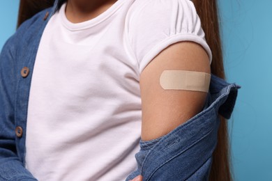 Photo of Girl with sticking plaster on arm after vaccination against light blue background, closeup