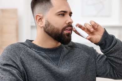 Photo of Medical drops. Young man using nasal spray indoors