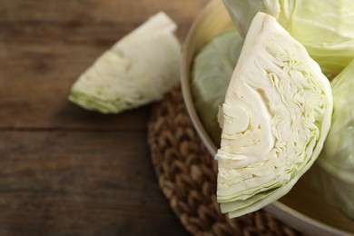 Photo of Fresh ripe cabbages in bowl on wooden table, closeup. Space for text