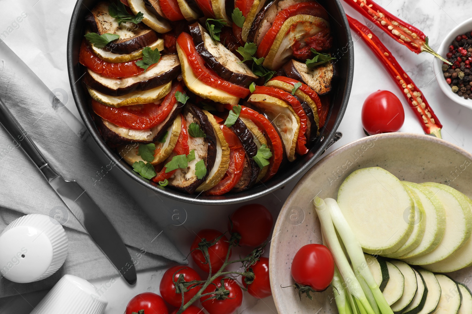 Photo of Delicious ratatouille, ingredients and knife on white table, flat lay