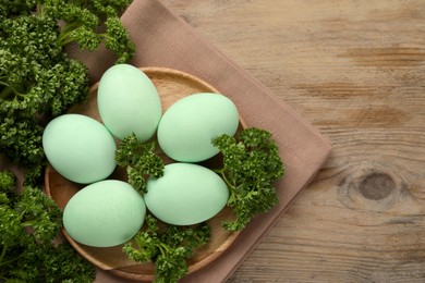 Photo of Turquoise Easter eggs painted with natural dye and curly parsley on wooden table, flat lay