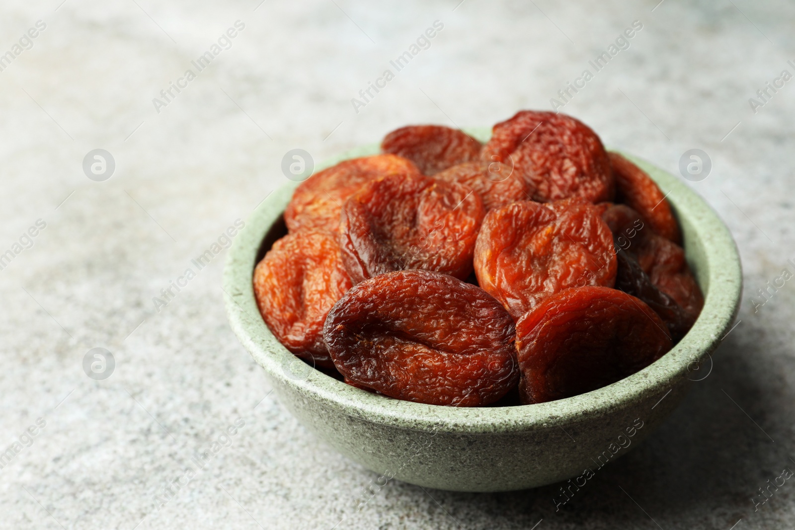 Photo of Bowl of tasty apricots on grey table, space for text. Dried fruits