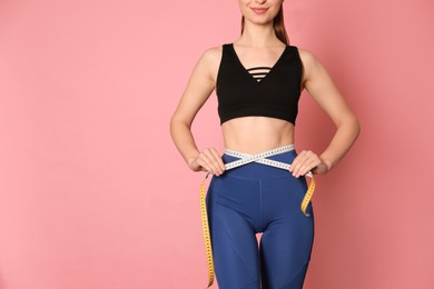 Photo of Happy woman in sportswear measuring waist with tape on pink background, closeup. Space for text
